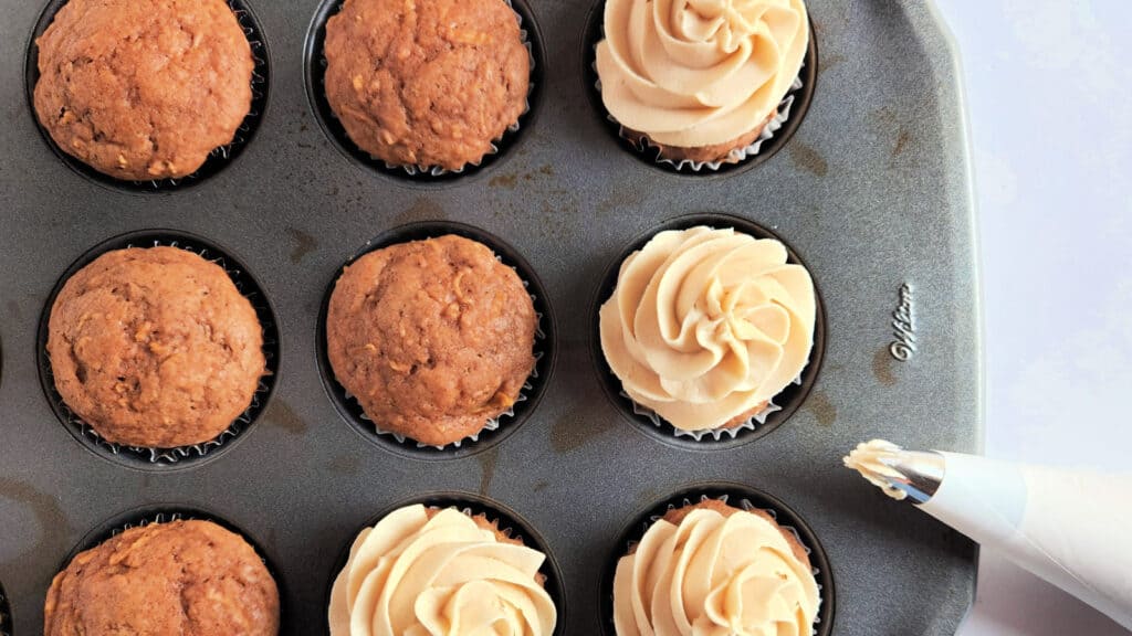 Apple cupcakes with frosting in a muffin tin.