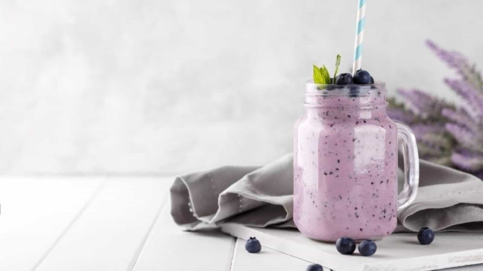 Blueberry Avocado Smoothie in glass mug with blue straw and napkin.