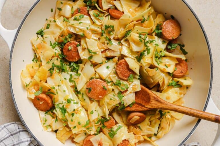 Cabbage and sausage in a pan with a wooden spoon.