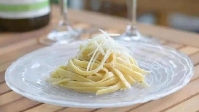 Image shows a plate with cacio e pepe in a neat pile topped with shaved parmesan cheese.