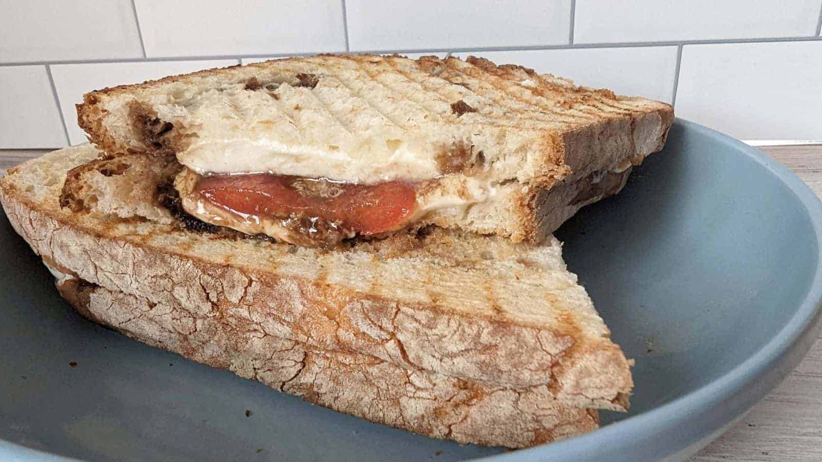 Image shows a sliced caprese panini on a wooden board with the melted cheese oozing out.