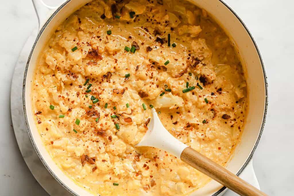 Cheesy cauliflower casserole in a pot with a wooden spoon.