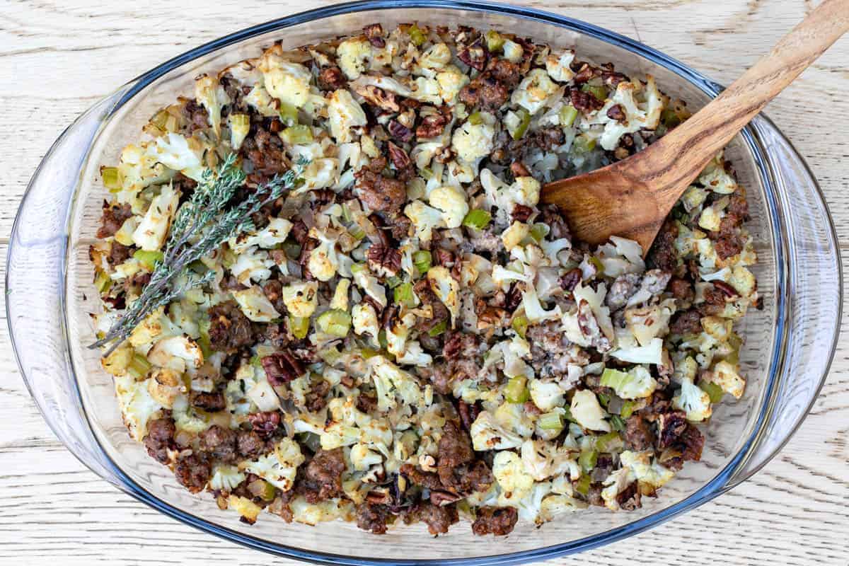 Baking dish with cauliflower sausage stuffing topped with thyme sprig.