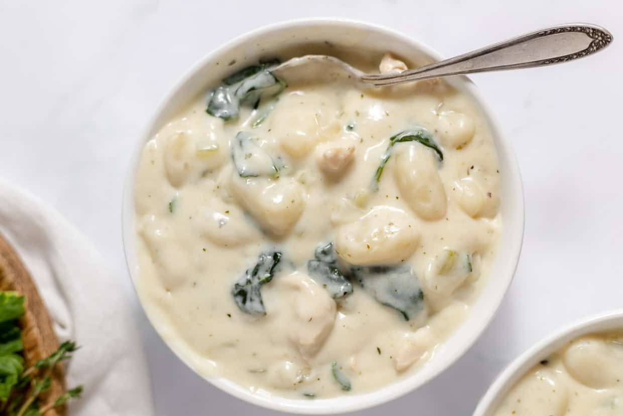 A bowl of chicken and gnocchi soup with a spoon in it.