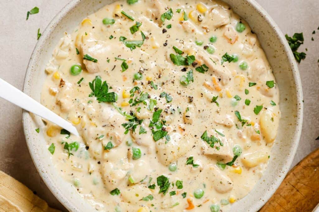 Chicken pot pie soup in a bowl with peas and carrots.