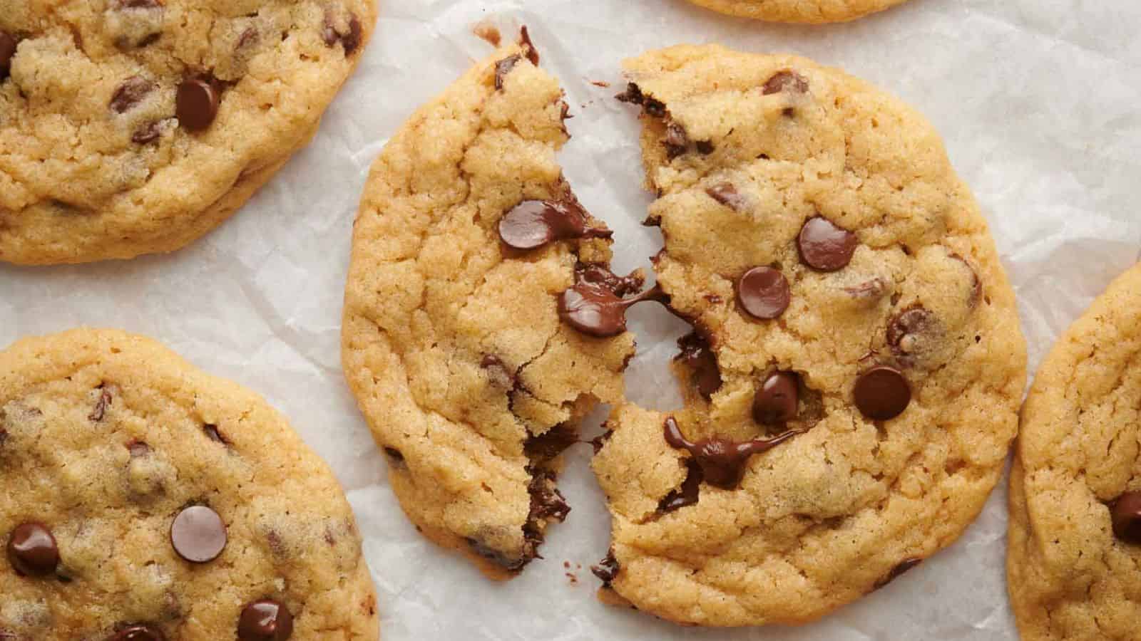 A hand holding a chocolate chip cookie on a cooling rack.