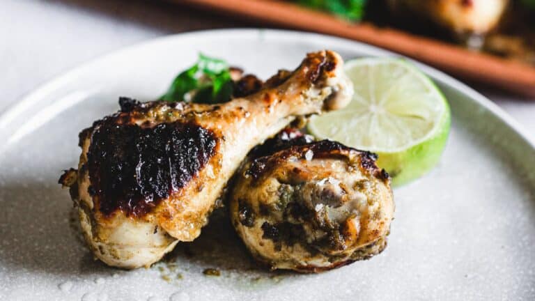 Grilled chicken leg with lime wedges on a white plate.