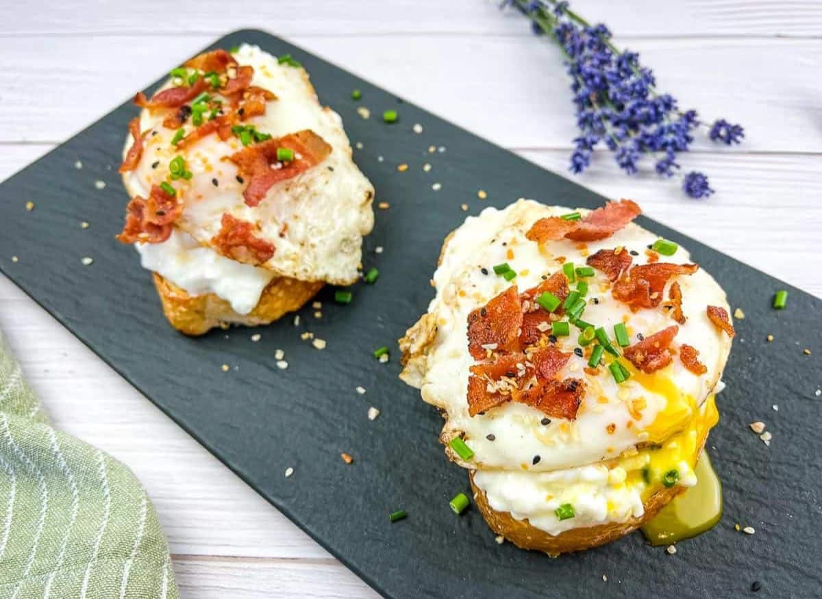 Two slices of Cottage Cheese Toast with Eggs & Bacon on a black platter.