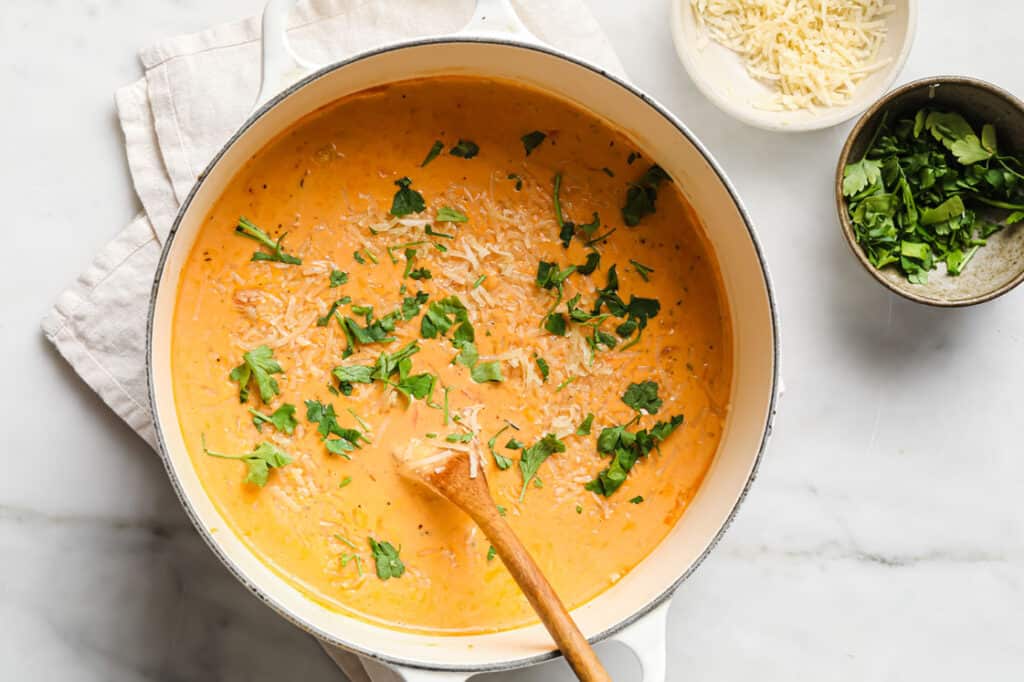 A pot of soup with creamy parmesan cheese and parsley.