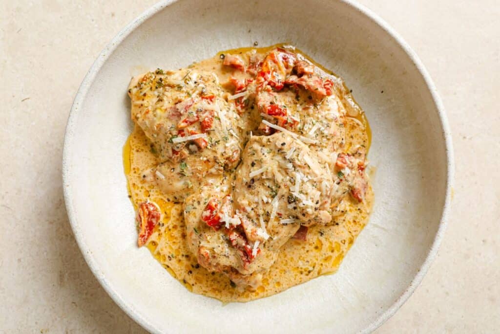 Chicken thighs with sun dried tomatoes in a white bowl.