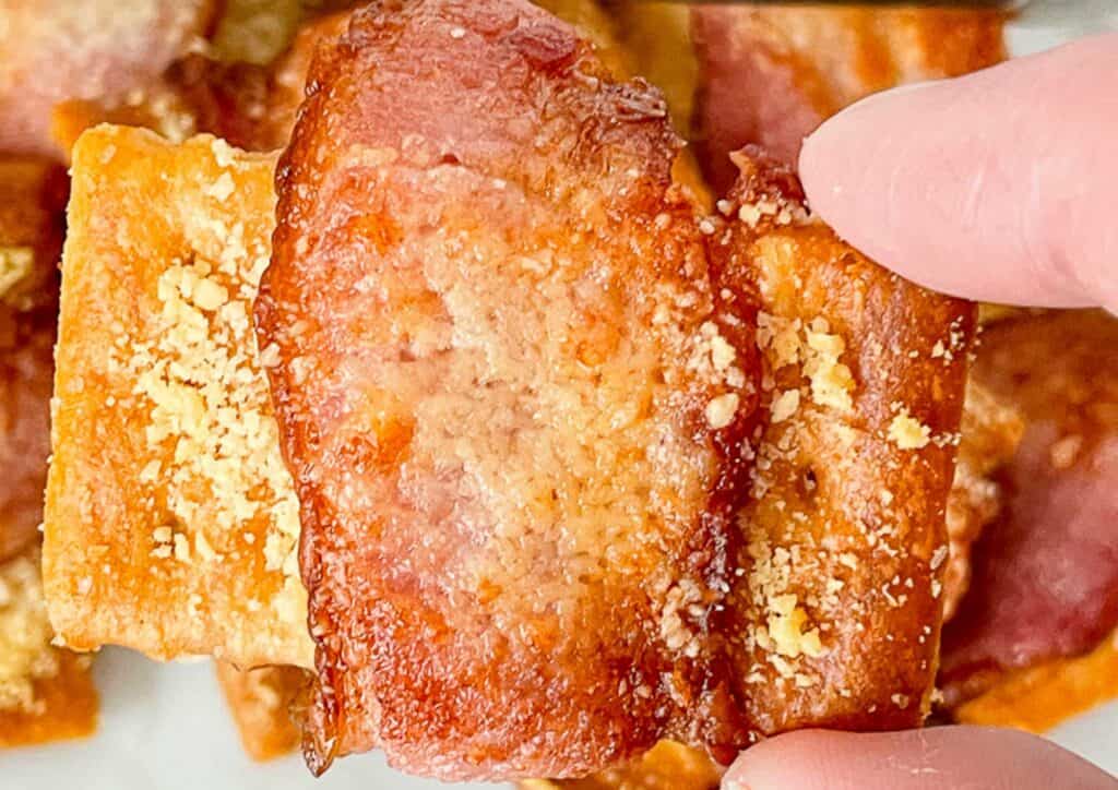 A person holding a plate with a piece of bacon, enjoying a warm winter dinner.