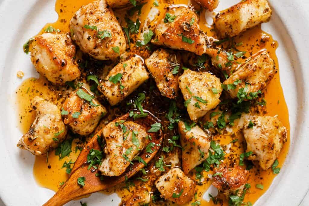 A plate of chicken bites in a garlic butter sauce with a wooden spoon.