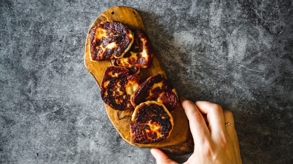 A hand holding a piece of fruit on a wooden board.