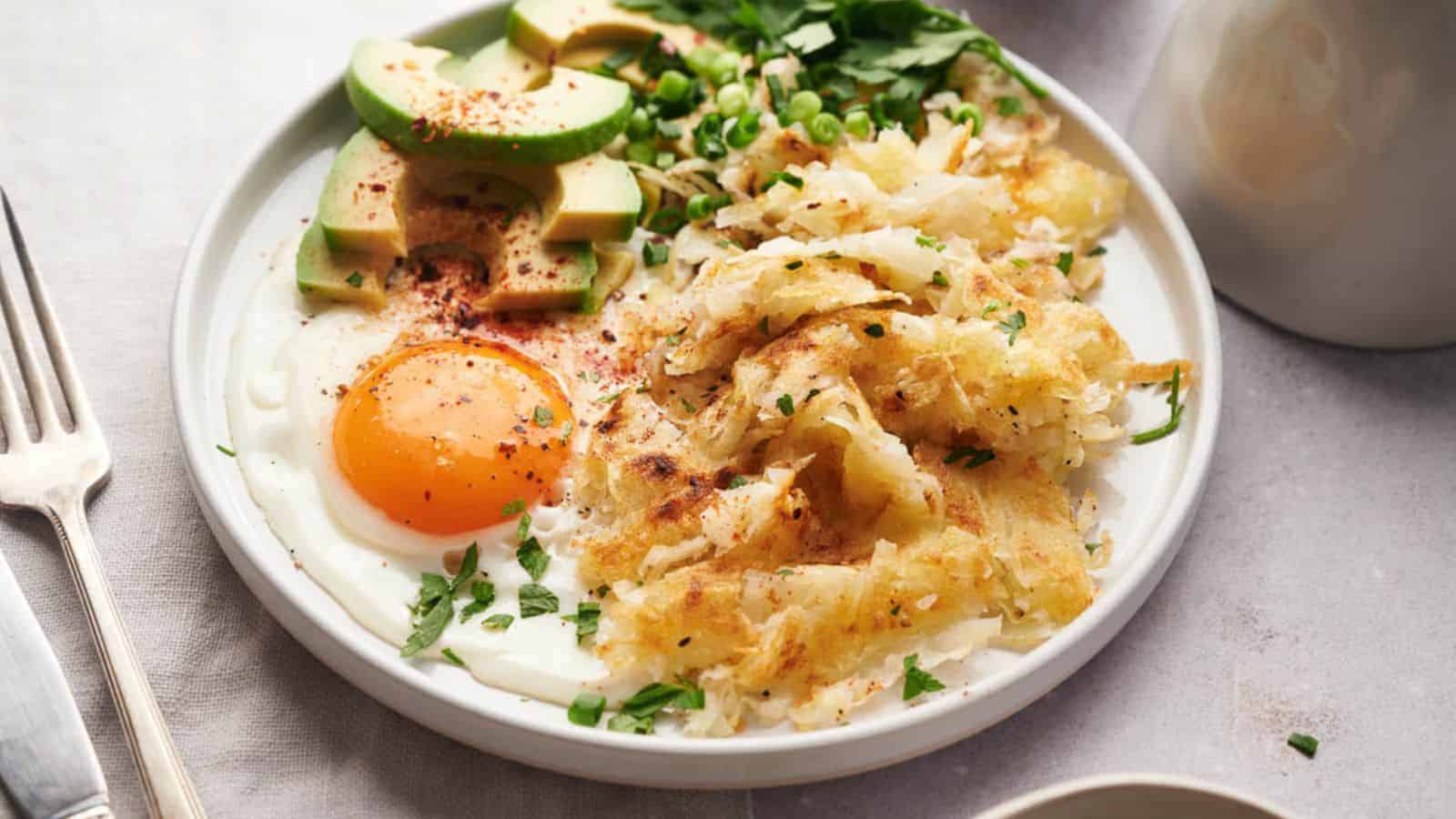 A plate with hash browns, eggs and avocado on a table.