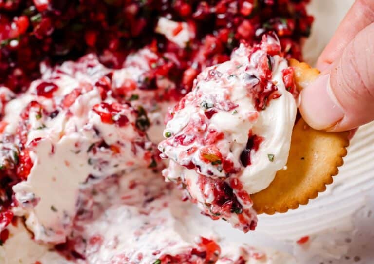 A person is dipping a cracker into a bowl of jalapeño cranberry dip.