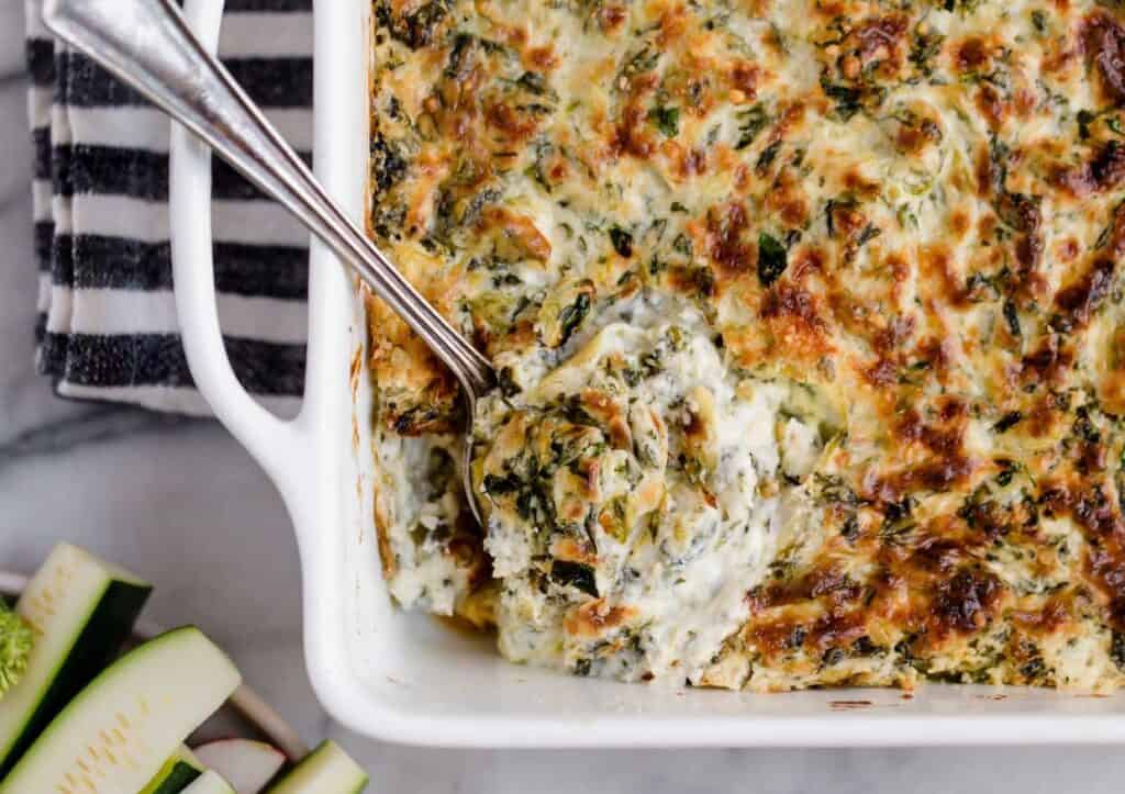 A dish of jalapeño spinach artichoke dip with a spoon.