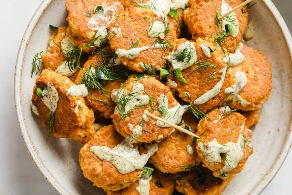 A plate of mini spicy canned salmon patties with dill sauce.