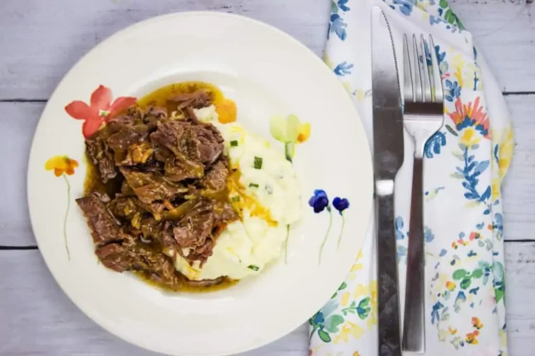 A plate of pot roast with bacon and mashed potatoes with gravy.