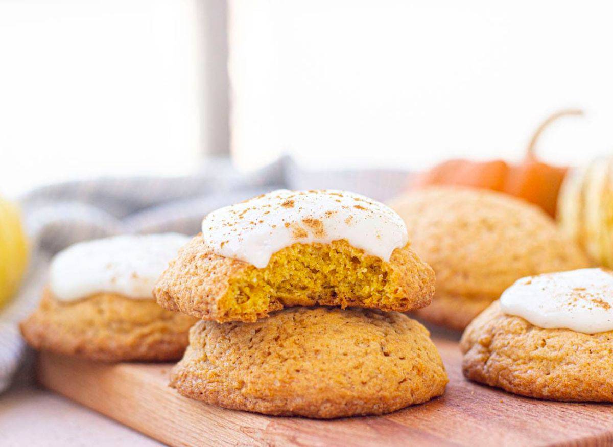 Pumpkin cookies with cream cheese frosting sitting on a board. Fresh pumpkin in the background.