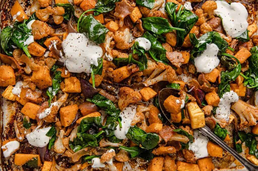 Roasted butternut squash with spinach and sour cream on a sheet pan.