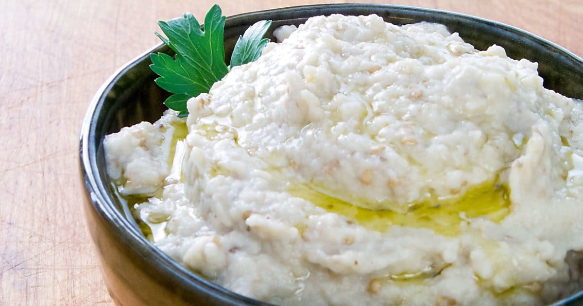 Baba ganoush garnished with olive oil and parsley in green bowl.