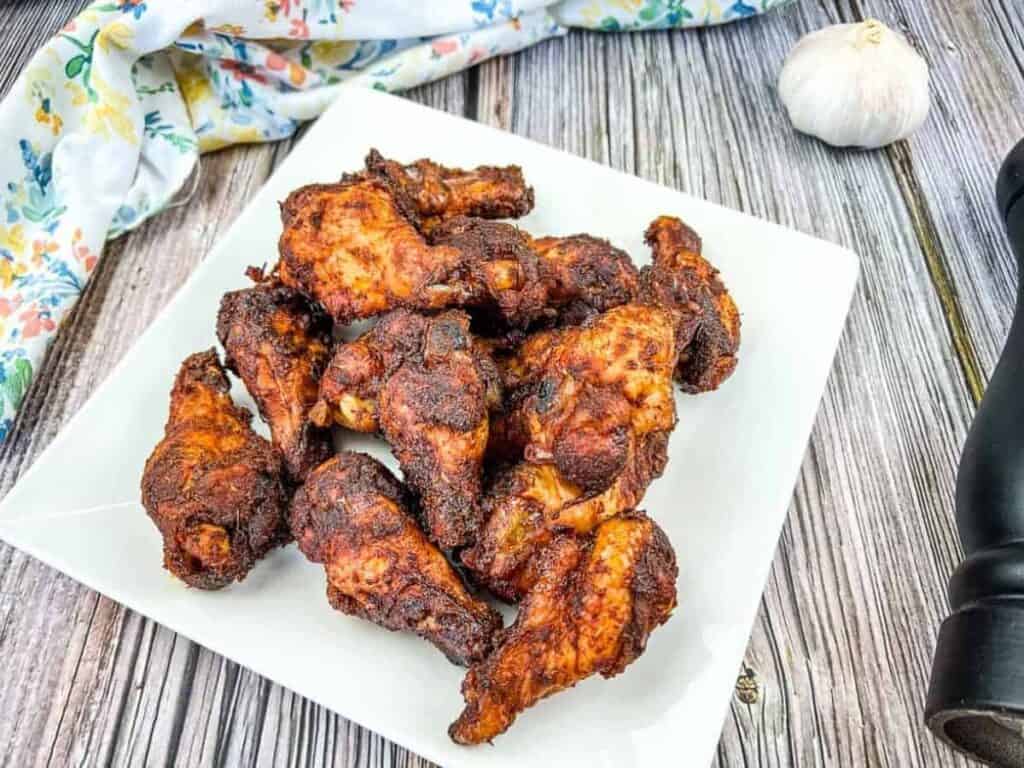 Bbq chicken wings on a white plate with garlic.