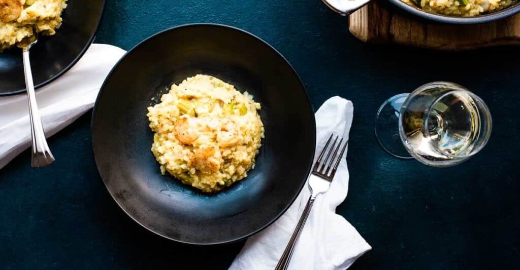 Two bowls of risotto on a table next to a glass of wine.