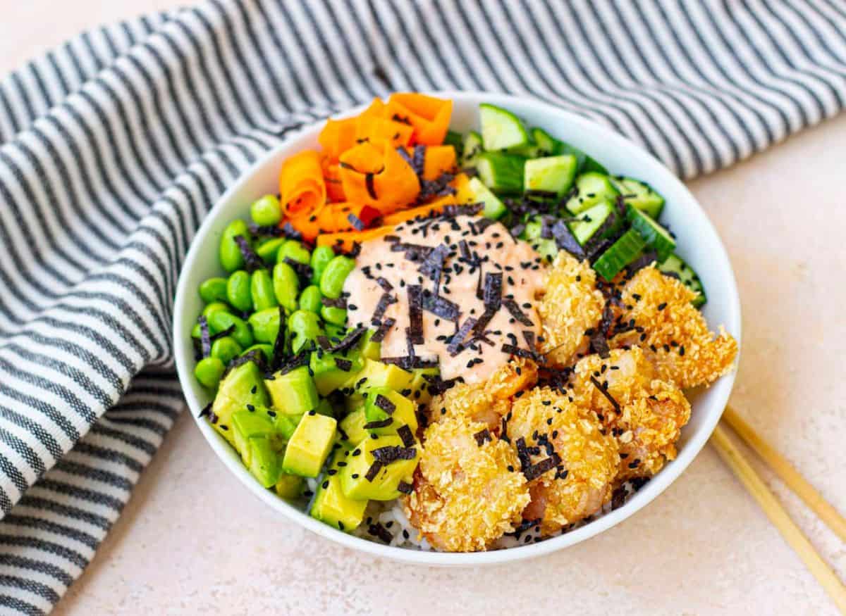 Sushi bowl with vegetables and chopstick seating next to the bowl.