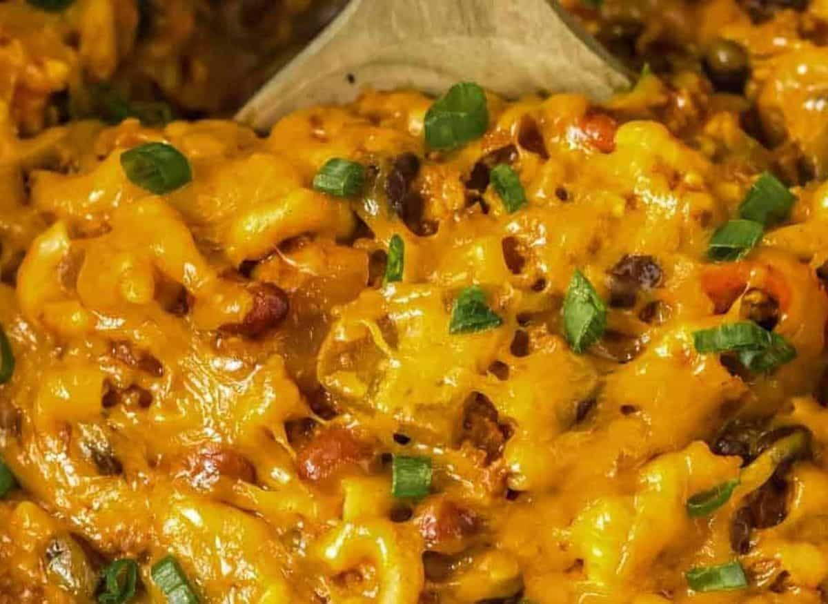 Cheese covered slow cooker chili mac in the crock pot with a wooden spoon.