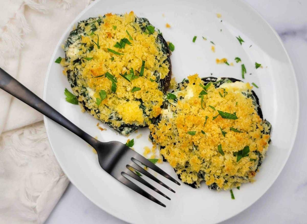 Two spinach stuffed portobello mushrooms sage scott on a plate with a fork.