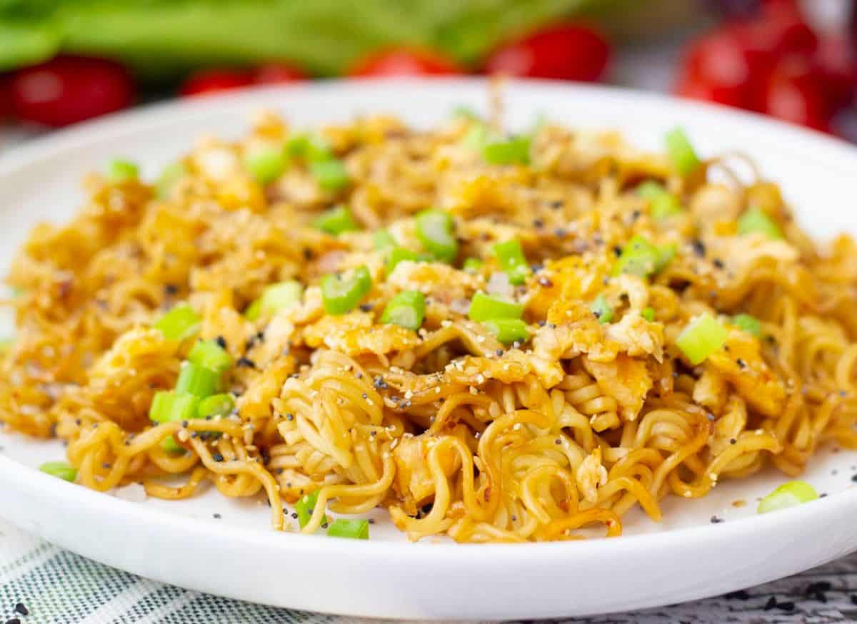 Cooked Ramen noodle in a white plate sprinked with fresh vegetable.