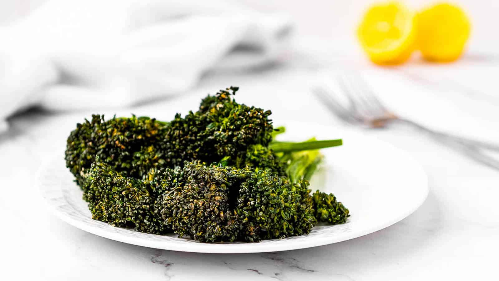 Air fried broccolini on a plate with lemons in the background.