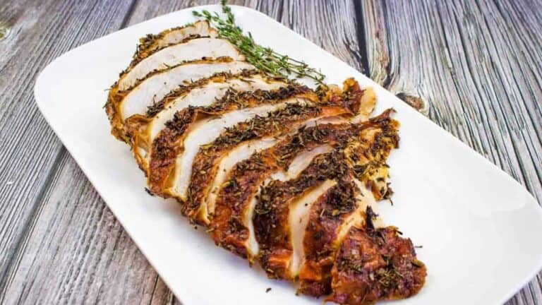 Sliced turkey on a white plate with sprigs of thyme.