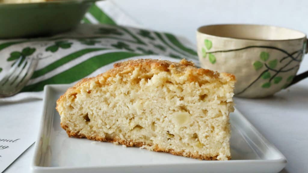 Apple scone slice on a white plate and a tea cup next to it.