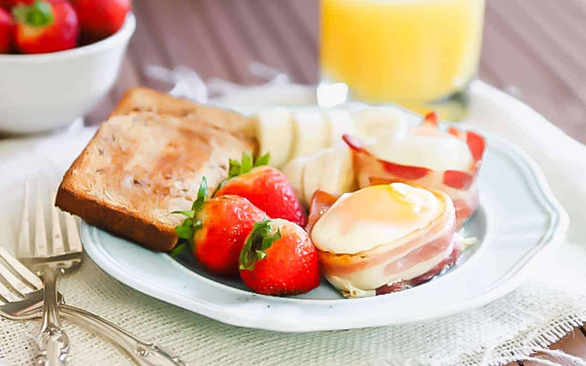 Bacon wrapped egg cups on a plate with toast and strawberries.