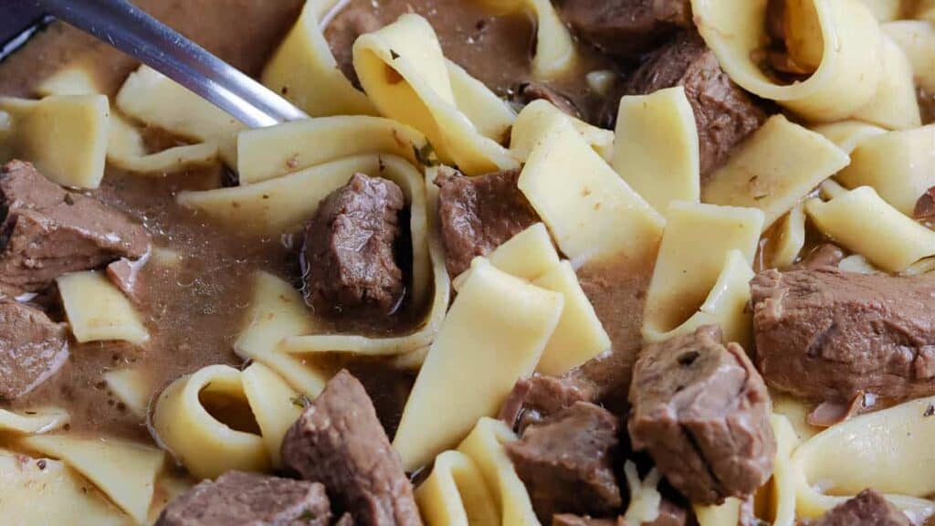 A bowl of beef stew with noodles and a fork.