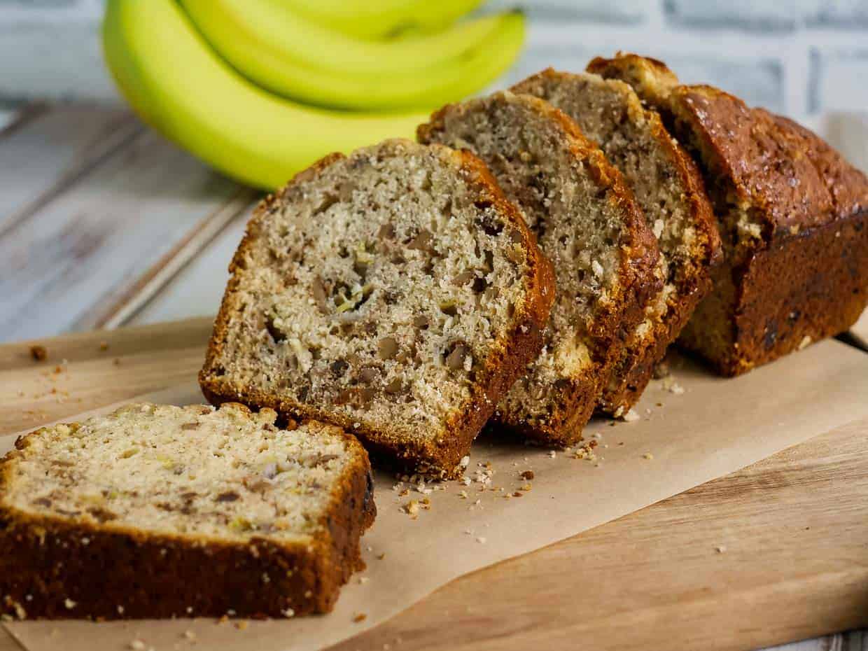 Sliced loaf of Bisquick banana bread on a cutting board with bananas in the background.