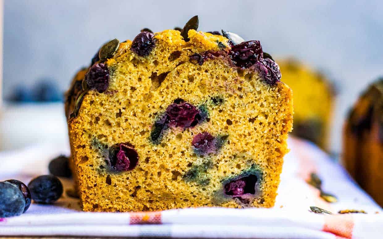 Blueberry pumpkin bread on a white towel with blueberries around.