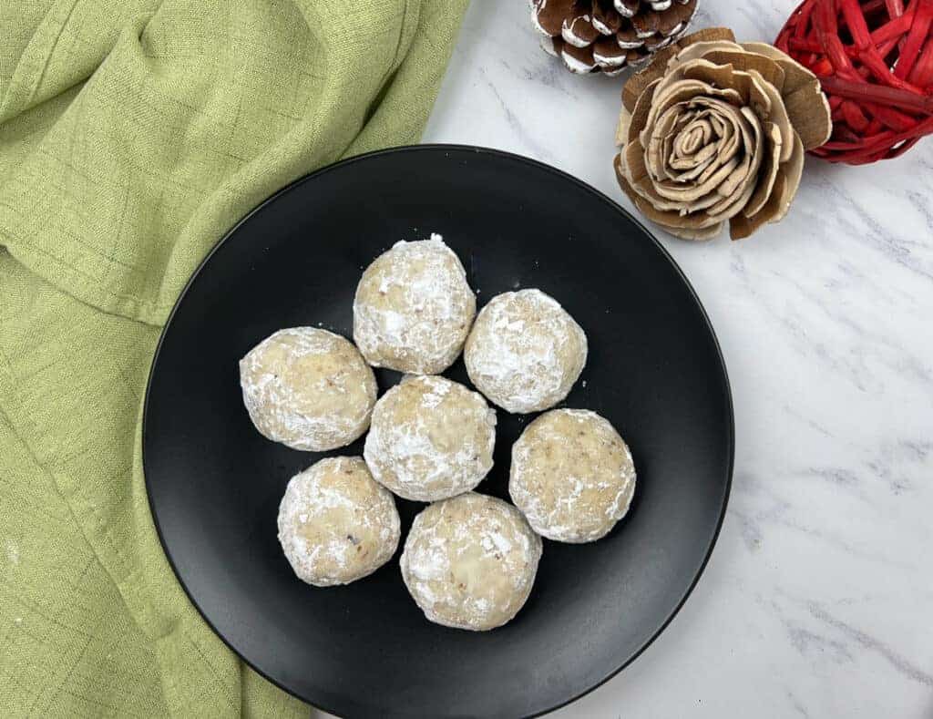 Three Pecan Butter Balls on a white plate with purple flower designs.