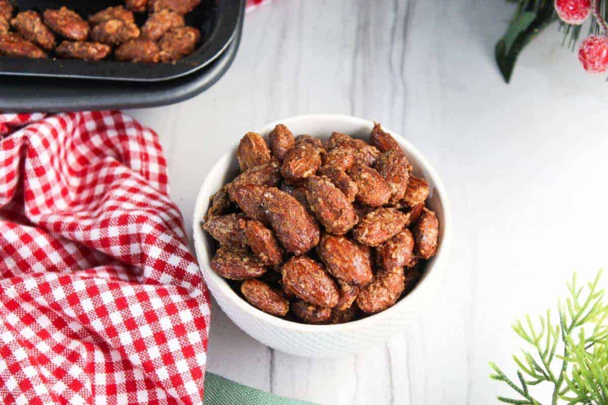 Roasted candied almonds in a white bowl next to a red checkered tablecloth.