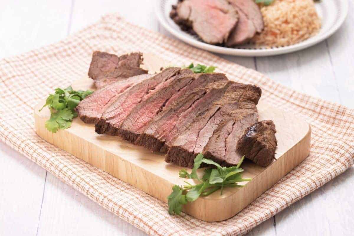 Slices of baked carne asada on small wood cutting board.