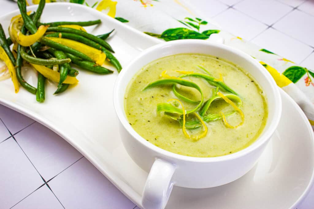 A white plate with a bowl of Cream of Asparagus Soup.