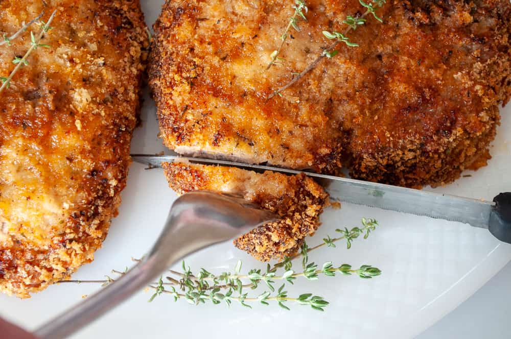 A knife cutting into a crispy pork chop.