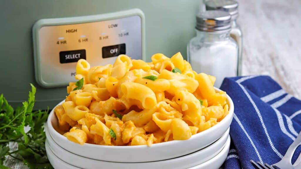 A bowl of macaroni and cheese in front of a slow cooker.