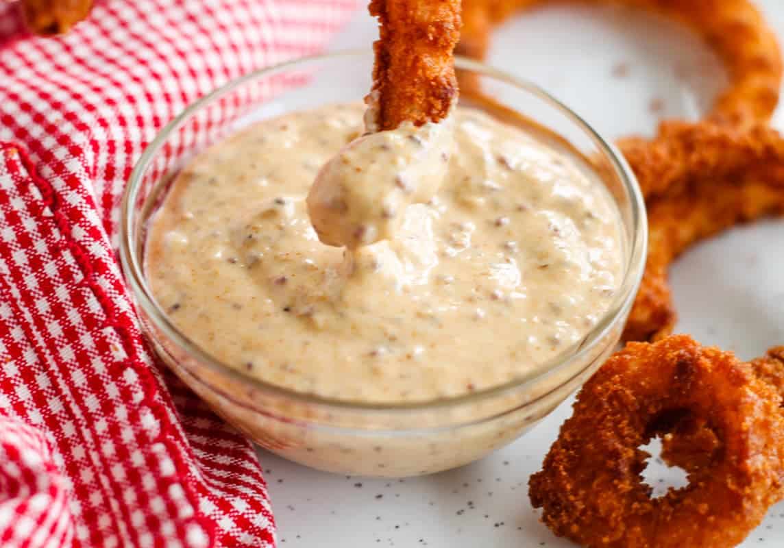 An onion ring being dipped into Spicy Dipping Sauce.