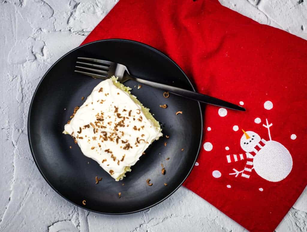 A piece of eggnog tres leches cake on a black plate with a fork.