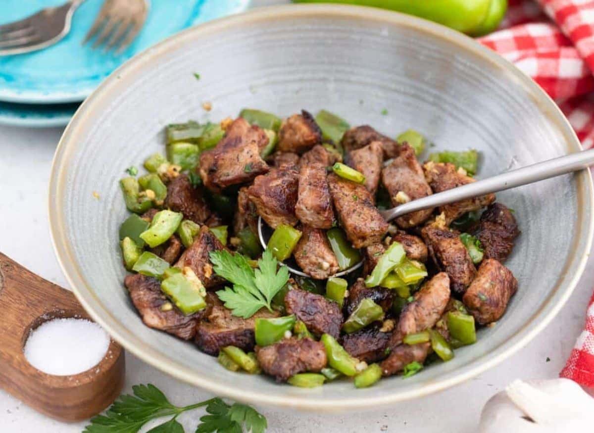 A bowl of meat and green peppers with a spoon.