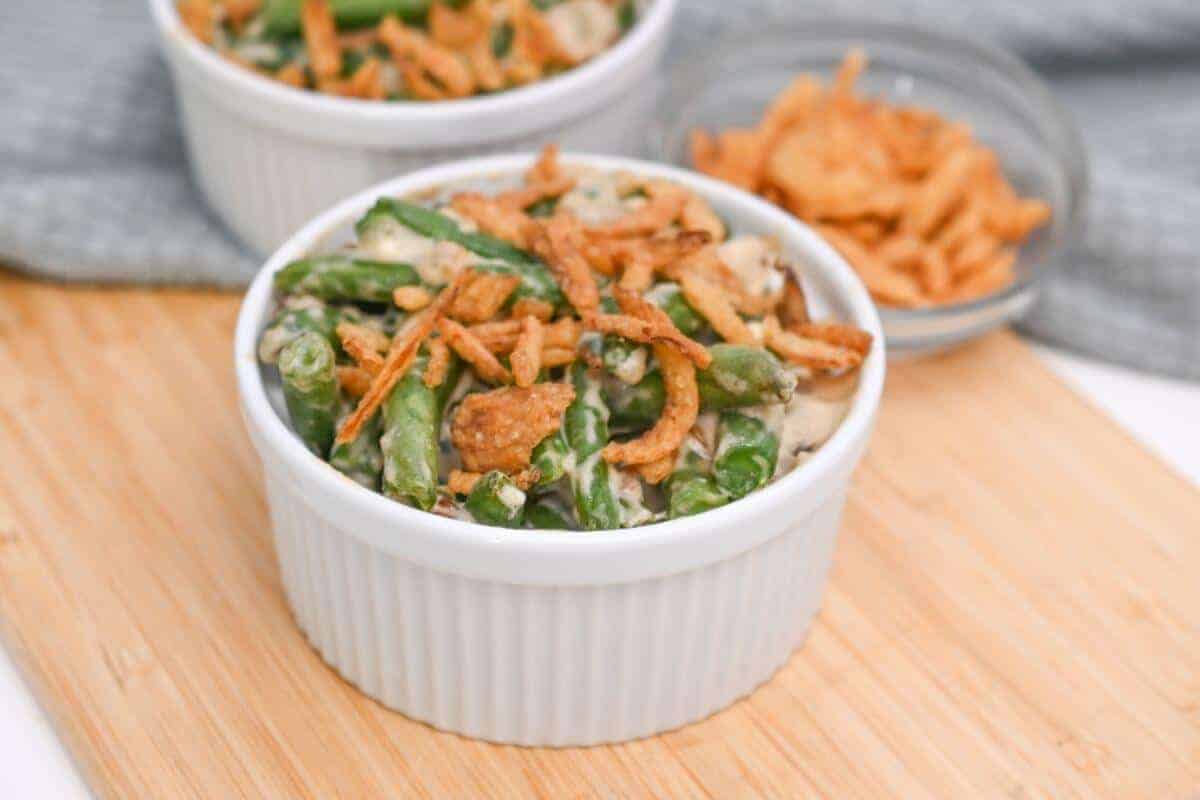 Two bowls of green bean casserole on a cutting board.