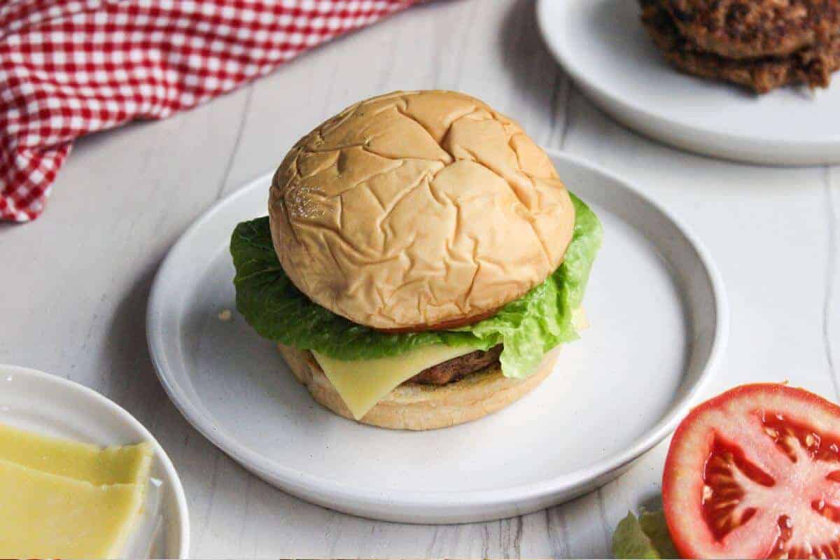 Two burgers on a plate with lettuce and tomatoes.