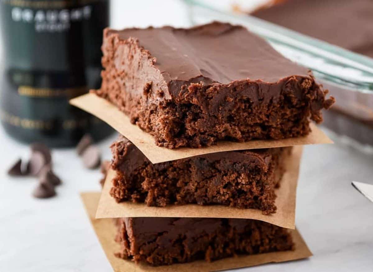 A stack of Guinness brownies with chocolate ganache next to a bottle of whiskey.